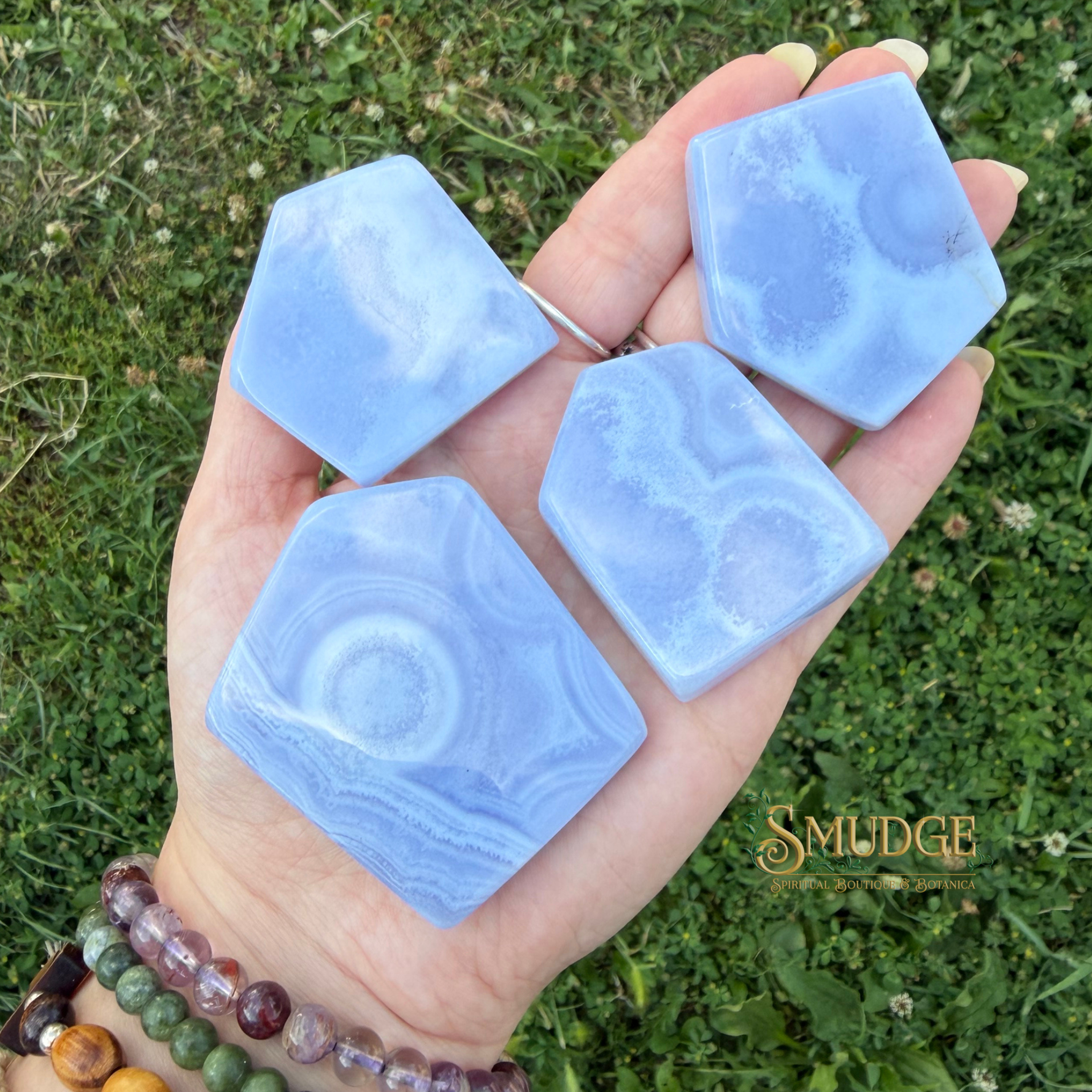 Slabs of blue lace agate on hand with grass in the background and Smudge logo