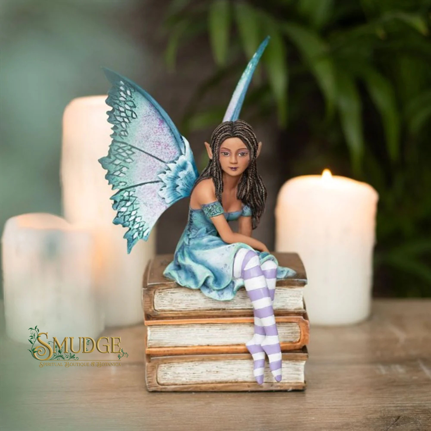 Fairy figurine with blue wings and striped socks sitting on books with candles in the background.