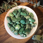 Bowl of green tumbled stones called buddstone in a white bowl on a wooden tabel.