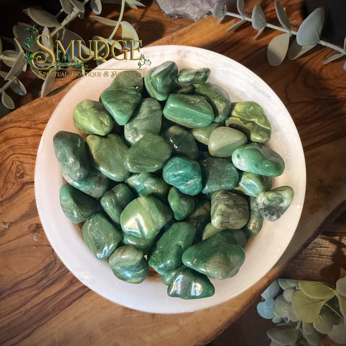 Bowl of green tumbled stones called buddstone in a white bowl on a wooden tabel.