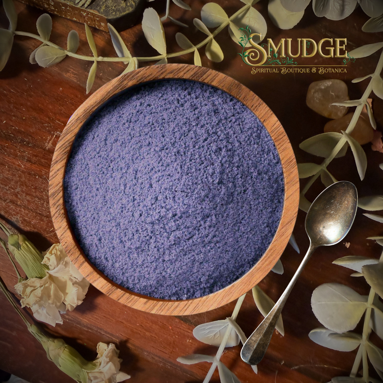 A wooden bowl filled with a textured purple powder, styled on a rustic wooden surface with eucalyptus leaves, crystals, a spoon, and the brand logo 'The Squeeze Botanicals' in the upper right.