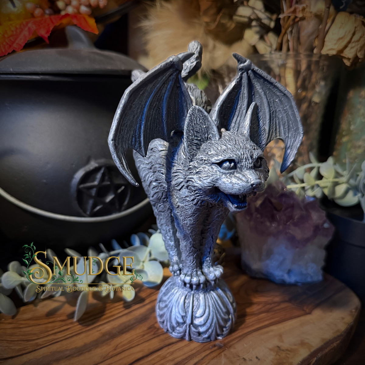 A gothic-style bat figurine with wings spread, standing on a carved pedestal. The bat is detailed with textured gray and silver tones.