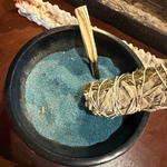 black bowl with blue coloured incense sand in it with a sage stick and palo santo. 