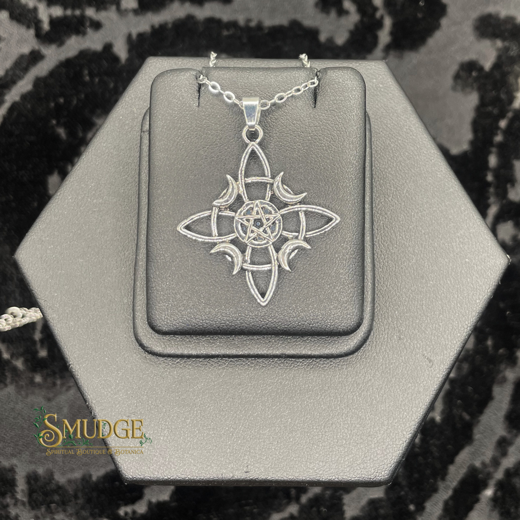 Silver pendant on a hexagonal gray stand with 'Smudge' branding.