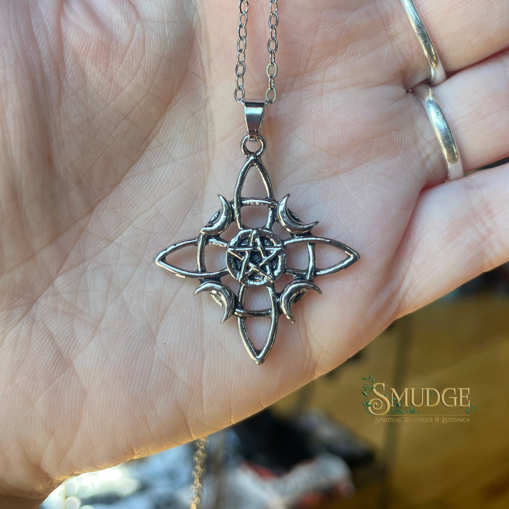 Silver pentagram pendant on a chain held in a hand, with 'SMUDGE' branding.