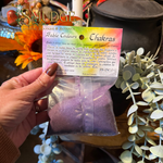 A hand holding a bag of purple sand in a bag labeled chakra sand.