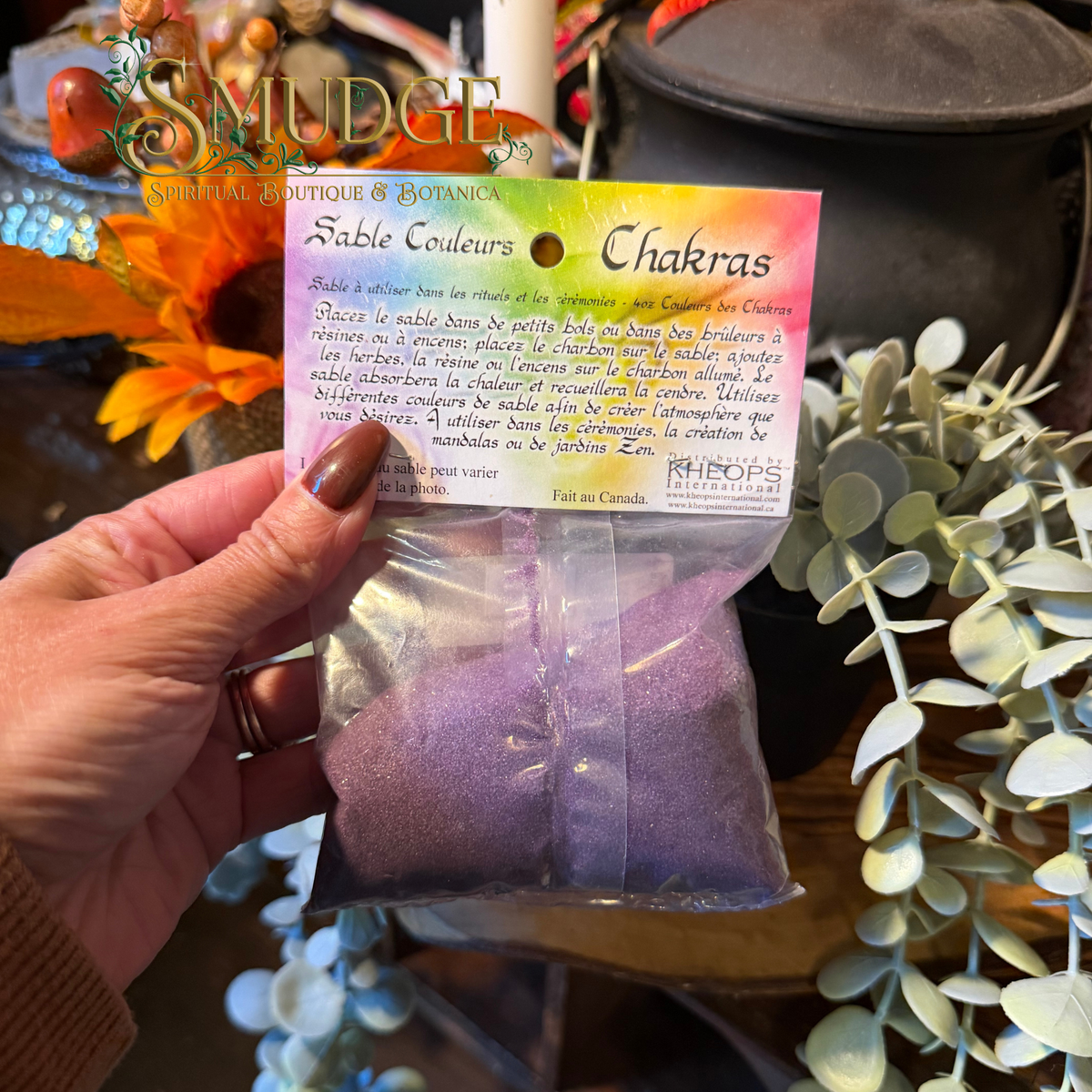 A hand holding a bag of purple sand in a bag labeled chakra sand.