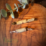 Two wrapped artisanal food items, likely caramel apples or candy-coated treats, wrapped in decorative brown paper, displayed on a polished wooden board with a green eucalyptus sprig and a 'Smudge' brand logo in the corner.
