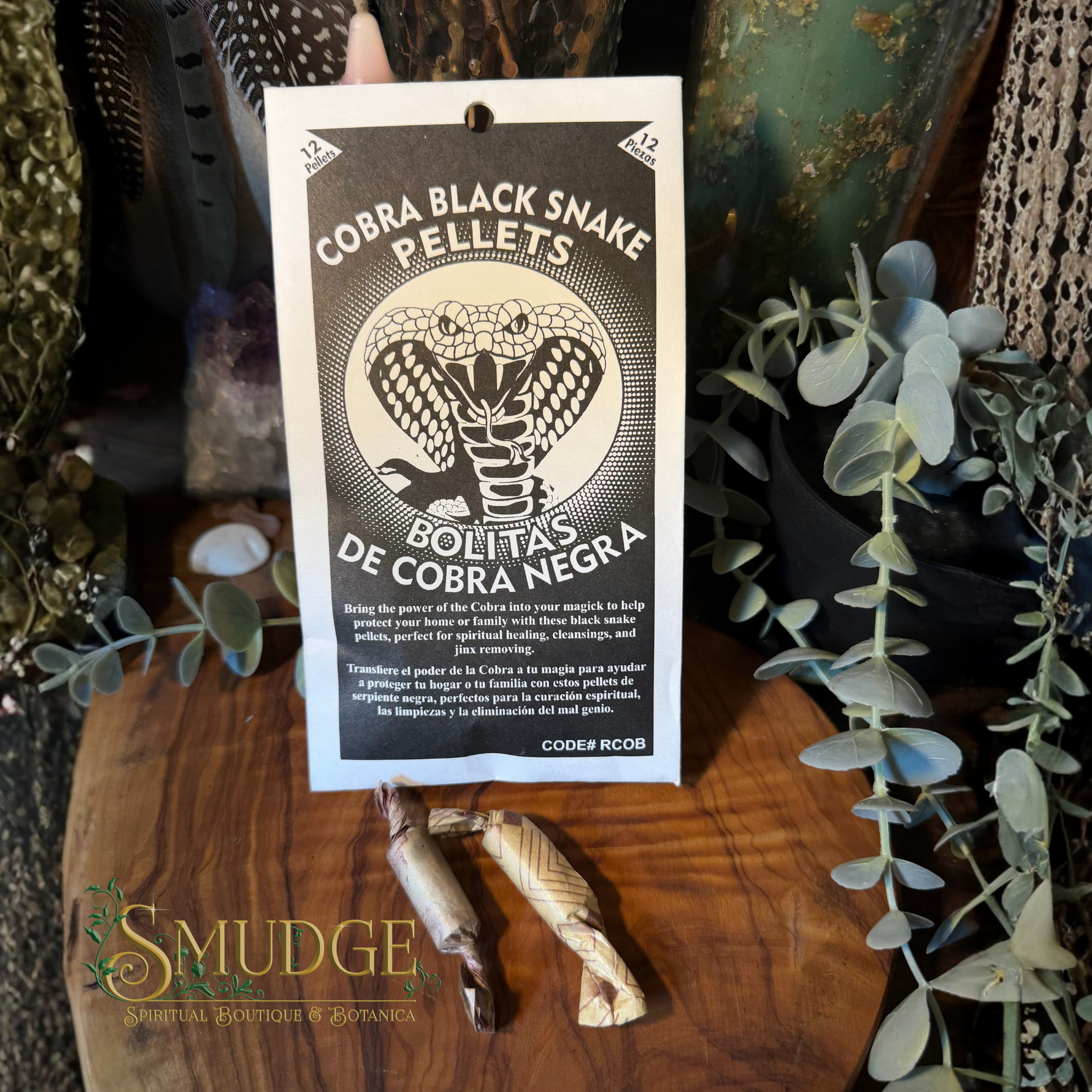 A package of Cobra Black Snake Pellets by Codep Roar is displayed on a wooden surface surrounded by green foliage and crystals. The white and black packaging features a prominent illustration of a cobra snake.
