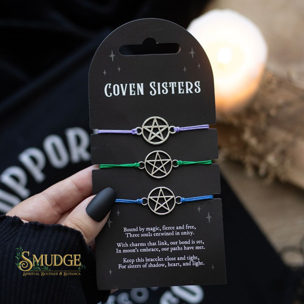 Three pentacle bracelets on a 'Coven Sisters' card held by a hand with dark nail polish.