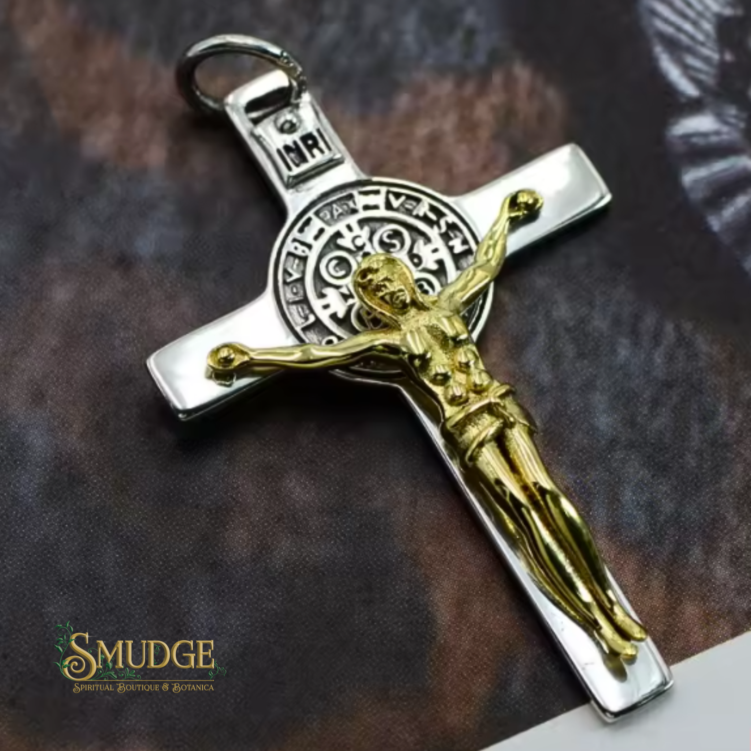 Silver cross pendant with gold Jesus figure on a textured brown background, branded 'Smudge'.