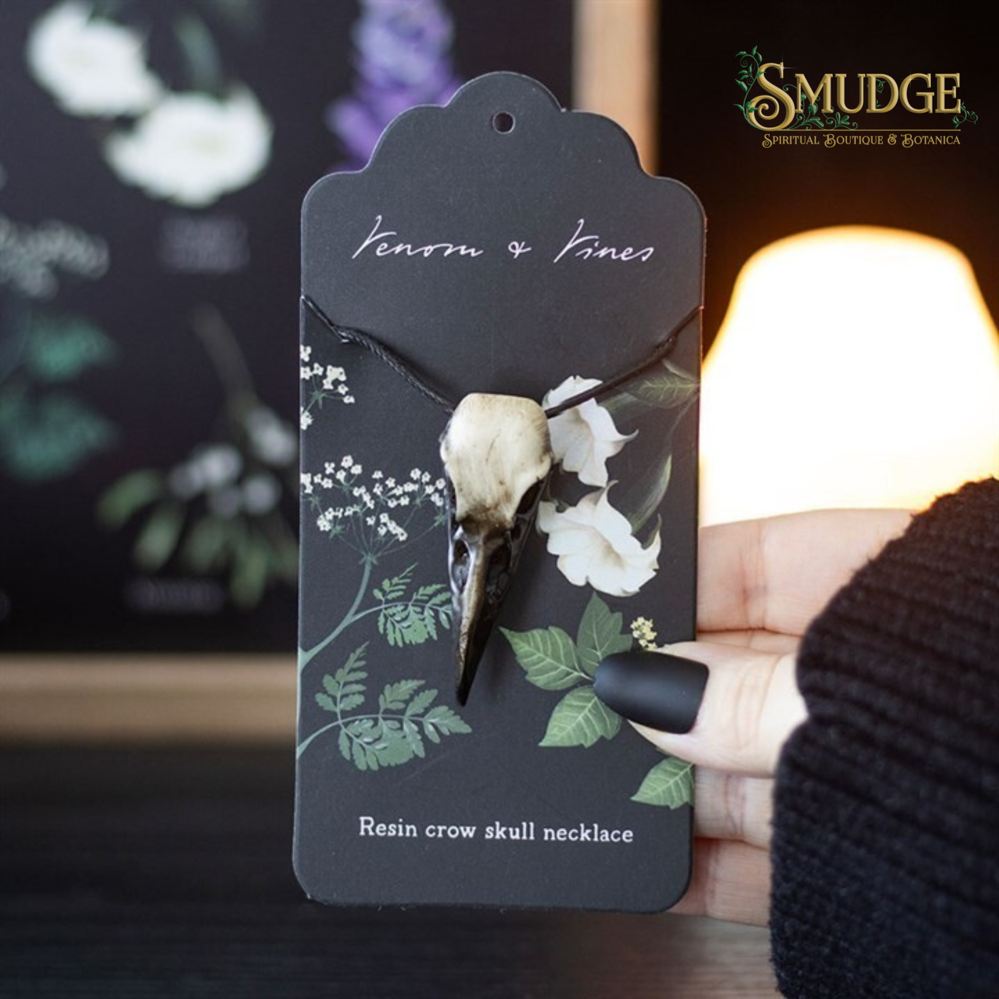 Hand holding Crow Skull Necklace from Venom and Vines on candlelit background with Smudge logo 