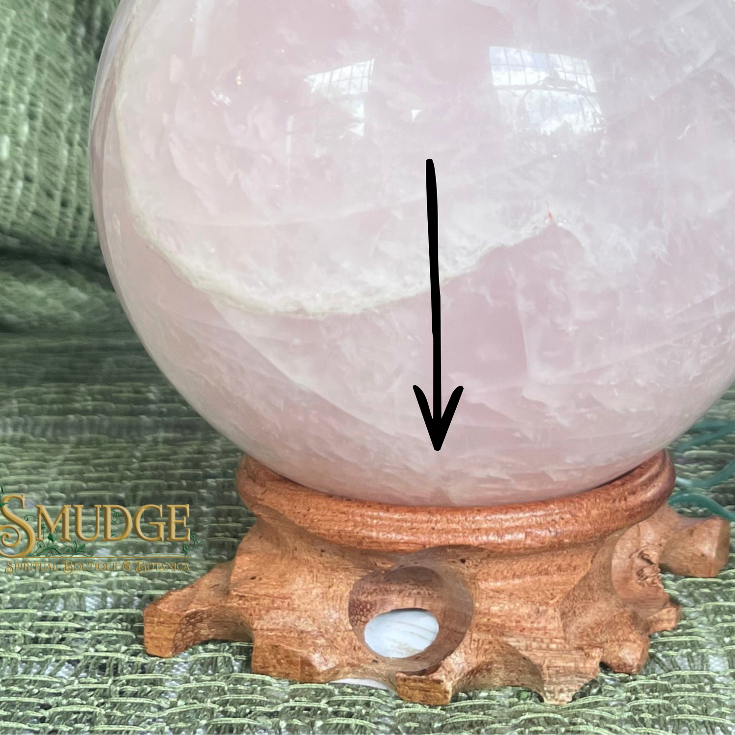 Rose quartz crystal ball on a wooden stand with 'Smudge' branding.