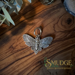 A death head moth silver earring on a wood background
