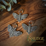 three silver death head moth charm earrings on a wooden background