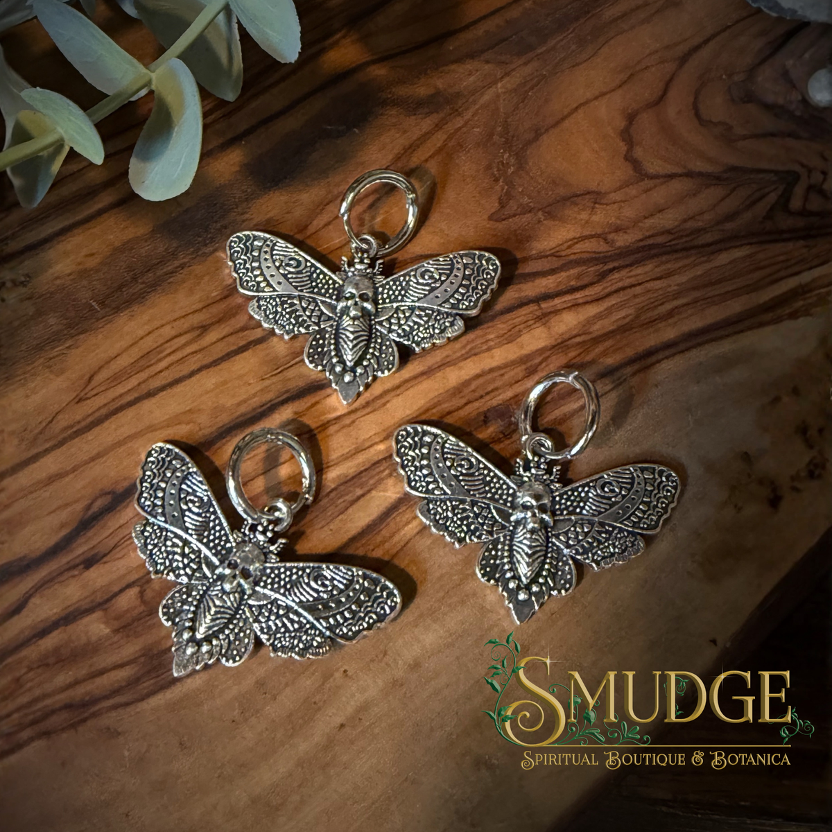 three silver death head moth charm earrings on a wooden background