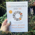 Book titled 'Decolonization and Me' held by a hand with green nail polish against a leafy background.