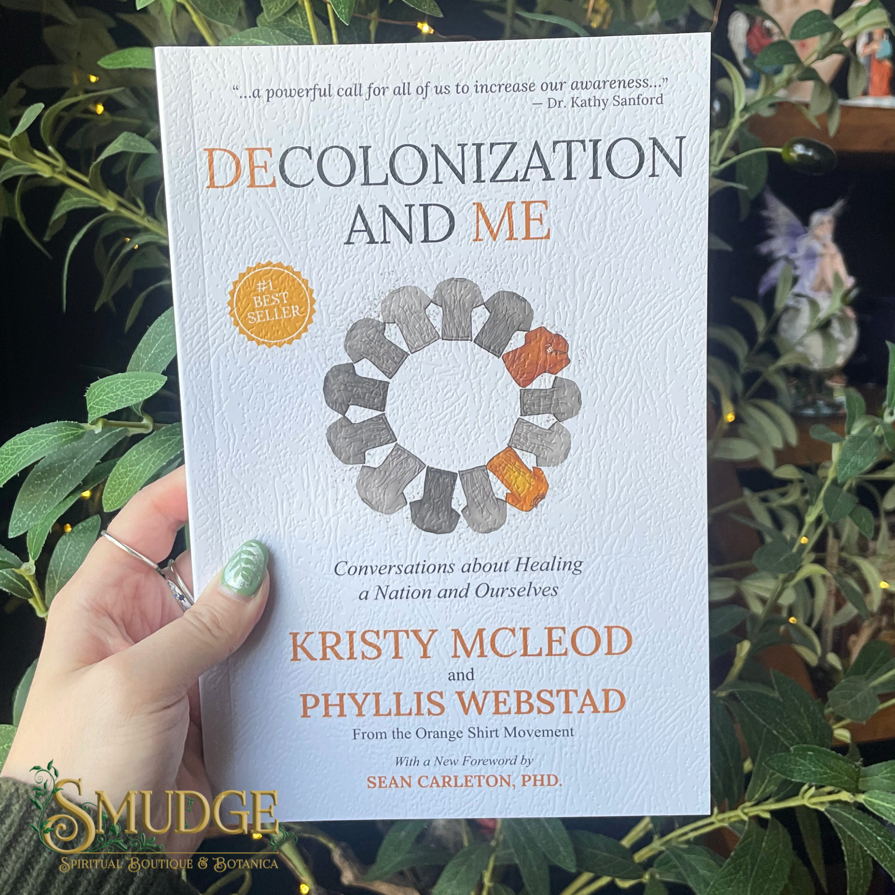 Book titled 'Decolonization and Me' held by a hand with green nail polish against a leafy background.