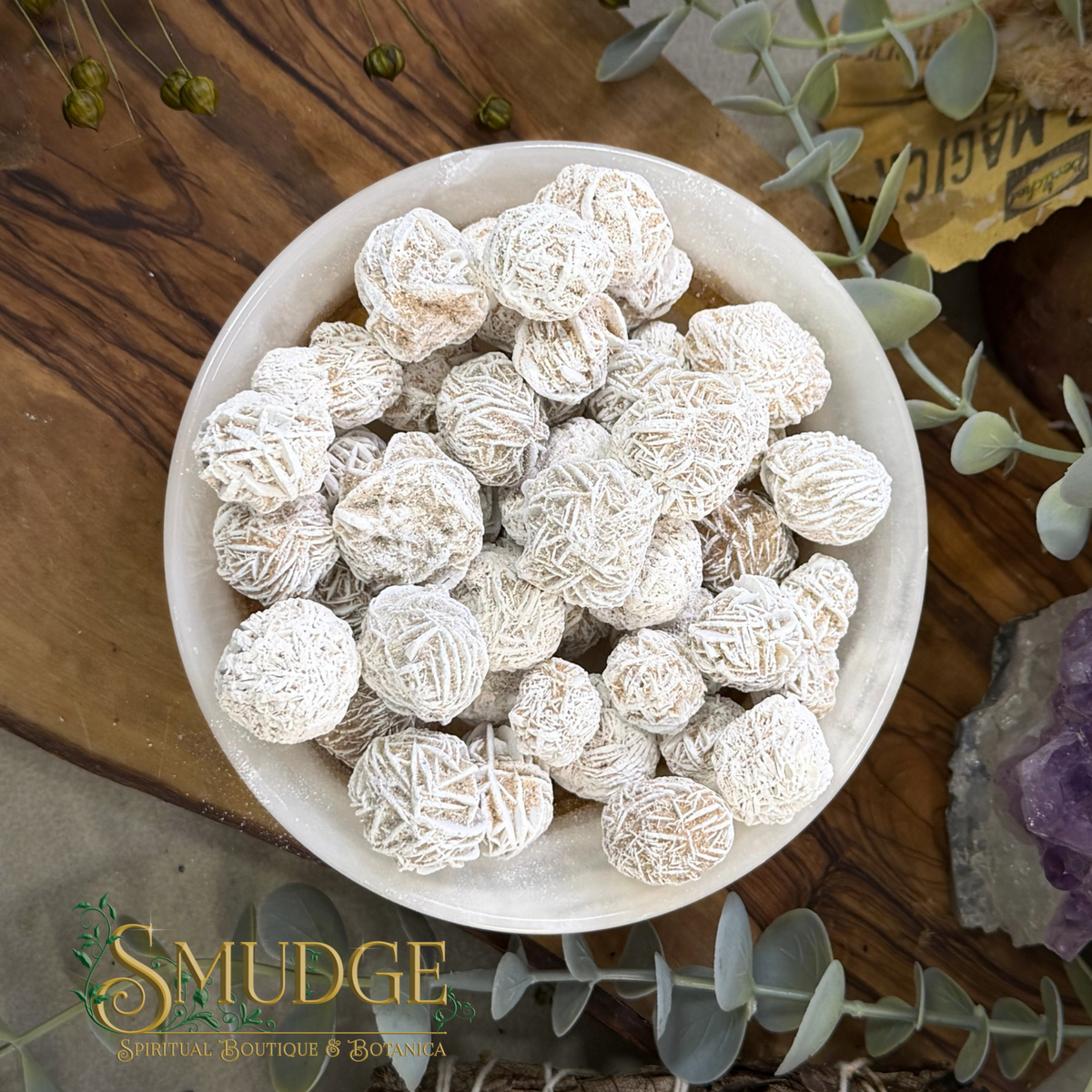 A bowl of white desert rose selenite crystals that look like roses. in a wood background.