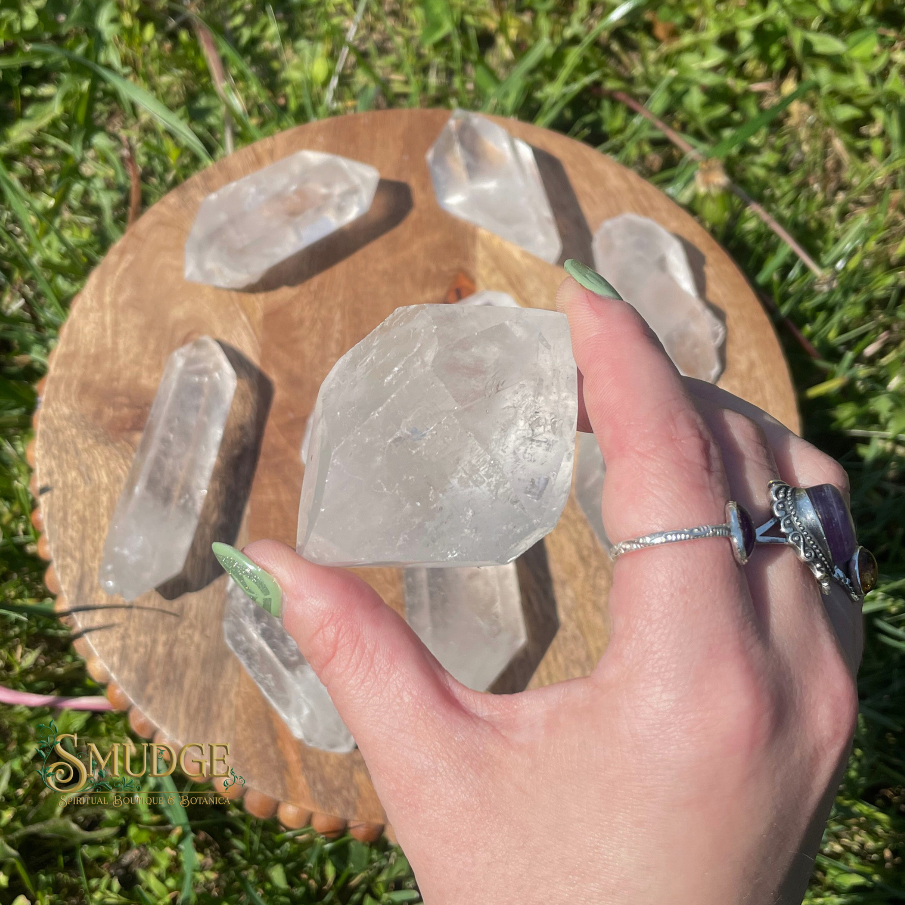 Hand holding a crystal over a wooden stand with crystals on a grassy background