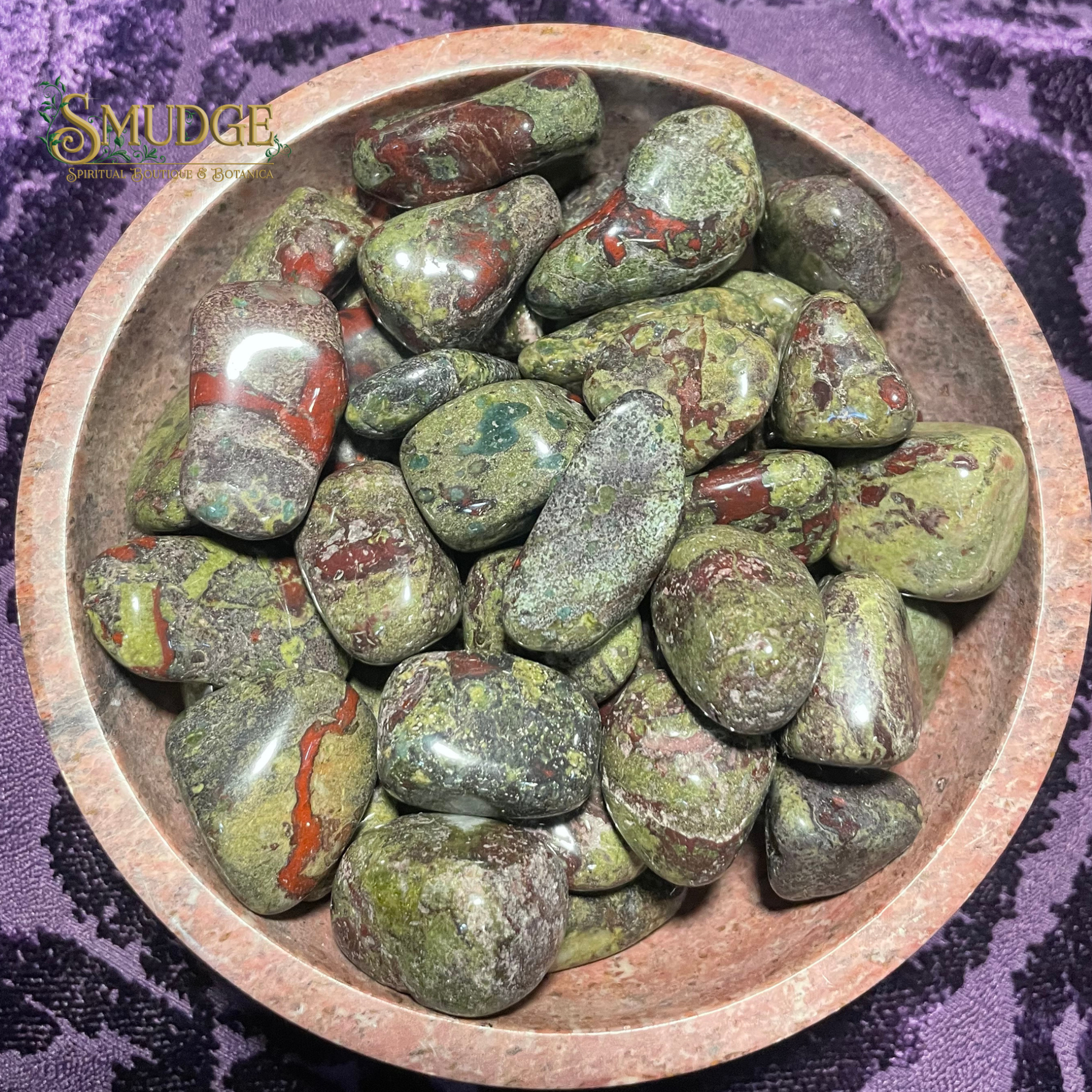 Wooden bowl filled with green and red stones on a purple fabric background