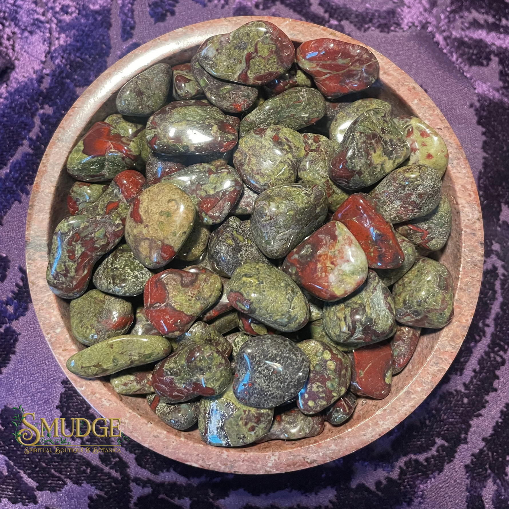 Bowl of polished gemstones on a purple fabric background