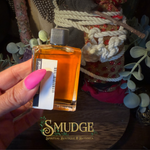 A hand with bright pink nails holds a small rectangular glass bottle filled with amber-orange liquid. The bottle has a silver cap and a white label with a barcode.
