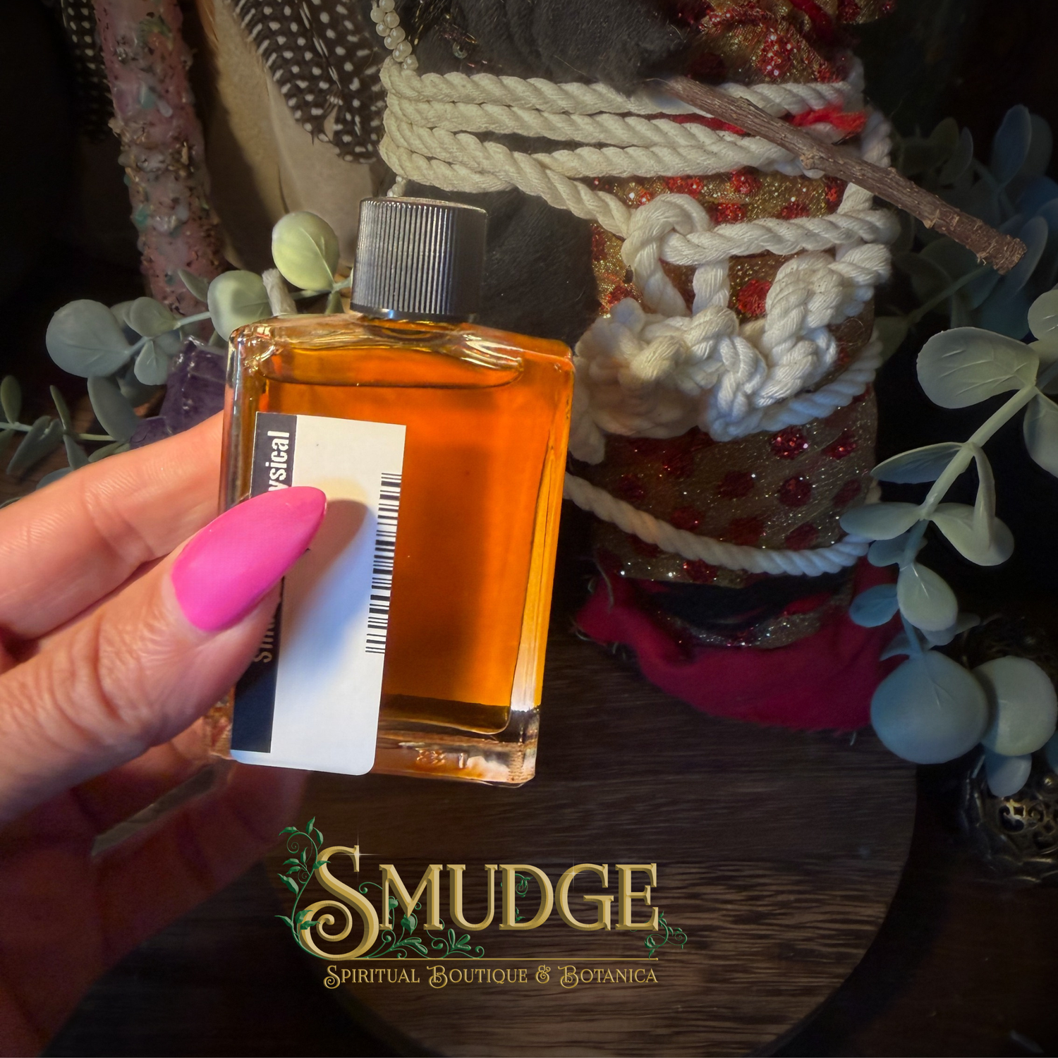 A hand with bright pink nails holds a small rectangular glass bottle filled with amber-orange liquid. The bottle has a silver cap and a white label with a barcode.