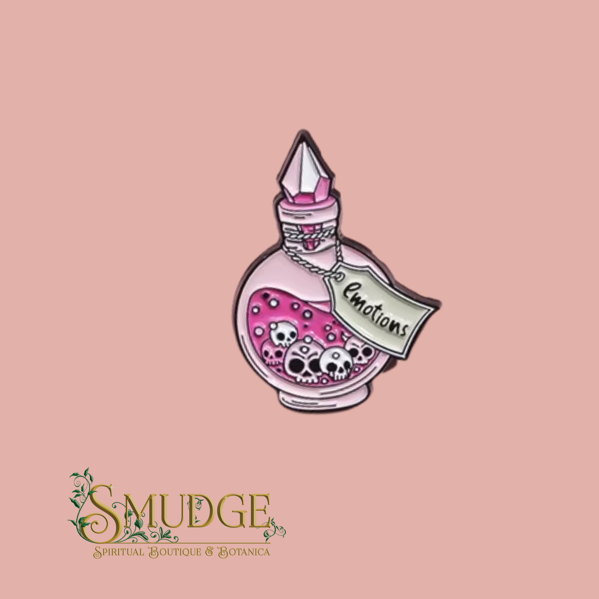 A pink and white enamel pin shaped like a potion bottle with skulls inside, featuring a tag that reads 'Emotions' and a gem-like cap, shown on a dusty pink background with the brand logo 'SMUDGE' at the bottom.
