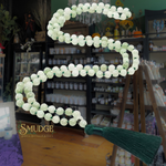 Decorative green beaded mala with tassel on a shelf in a store setting, featuring the brand 'Smudge'.