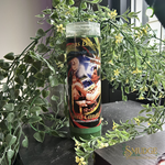 Successful Sales 7 Day Candle with a colourful label in front of green foliage.