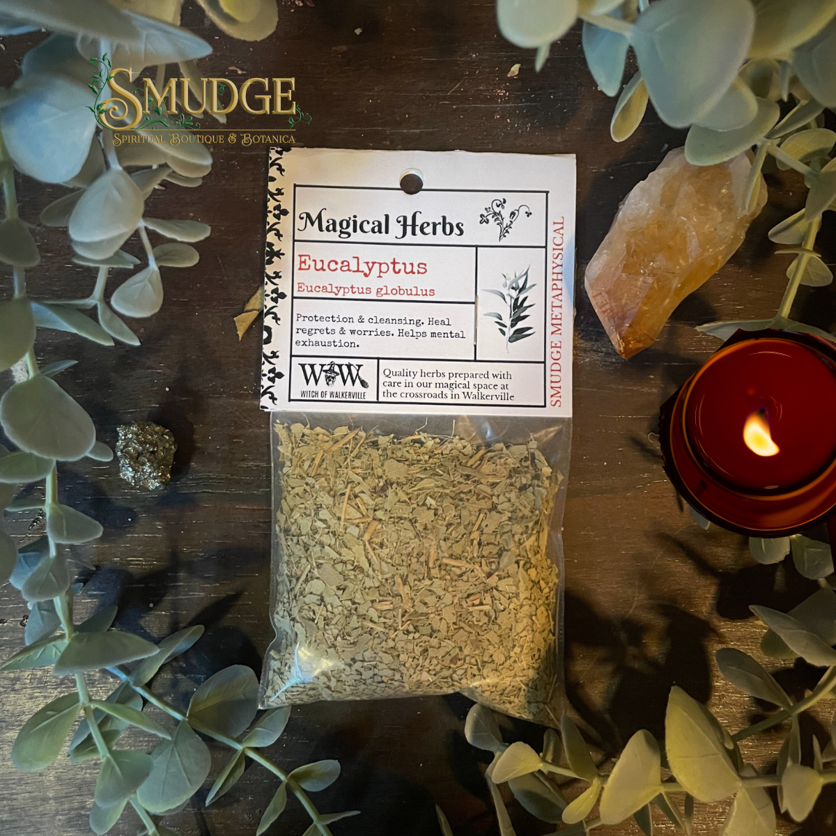 Bag of eucalyptus herbs with packaging on a wooden surface surrounded by eucalyptus leaves and a candle.