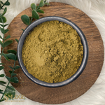 Bowl of green powder on a wooden plate with eucalyptus leaves, branded 'Smudge'.