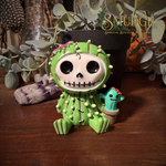 Furrybones prickle with a skeleton face smiling and a cactus costume. Sitting beside him is a baby cactus.