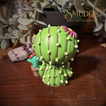 the back of the furrybones prickle figurine. a cactus costume with a purple flower on his head. A baby cactus sits beside him.