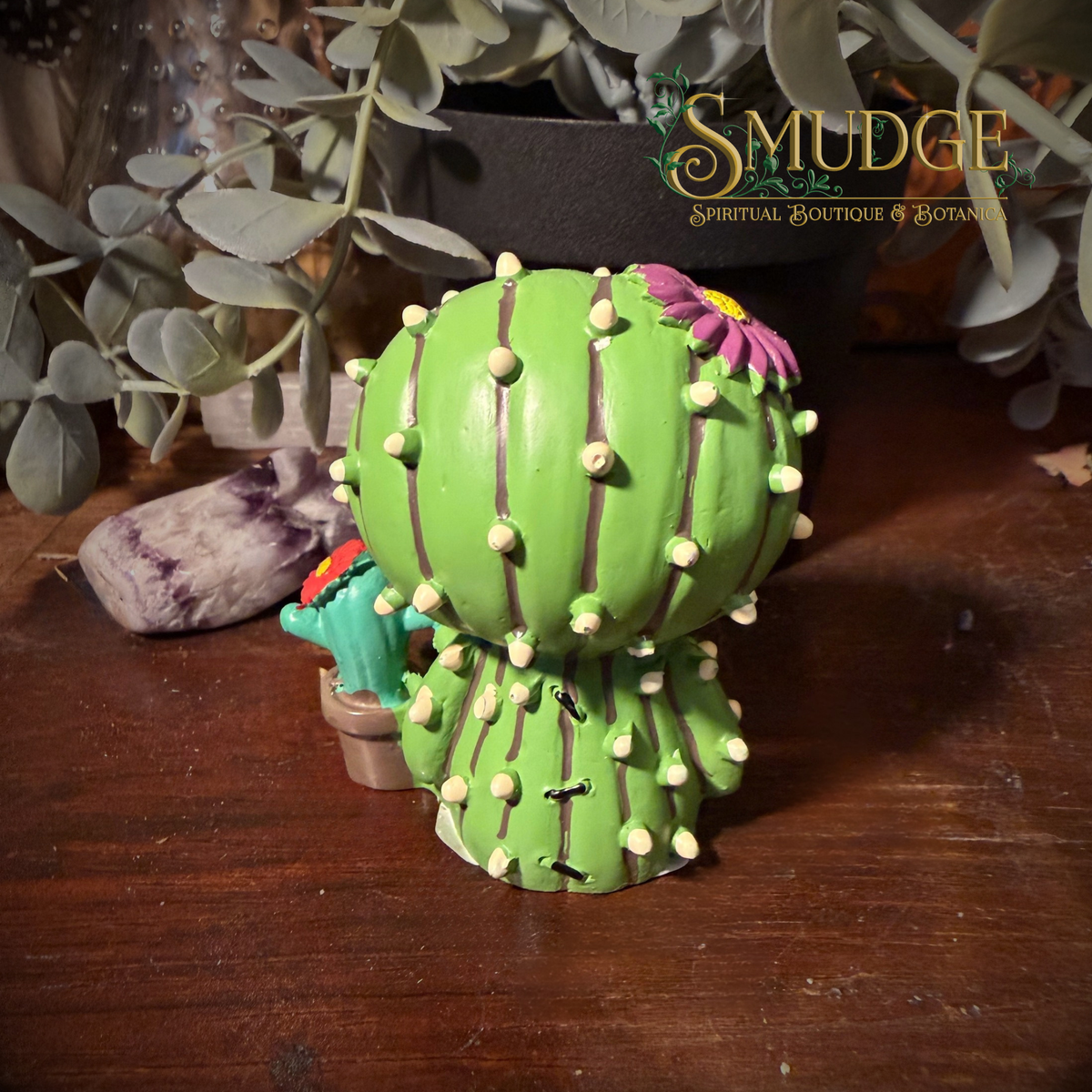 the back of the furrybones prickle figurine. a cactus costume with a purple flower on his head. A baby cactus sits beside him.