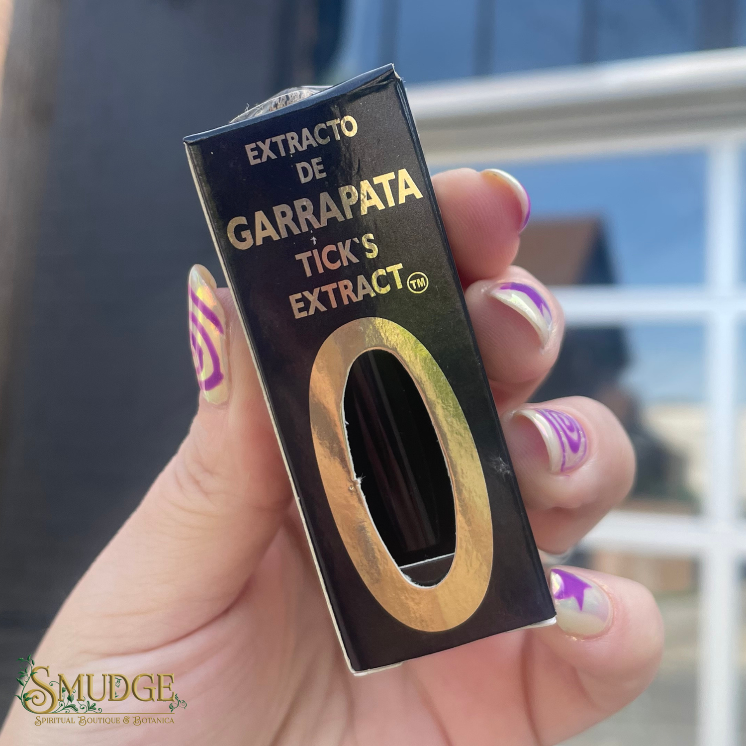 Hand holding a box of 'Extracto de Garrapata Tick's Extract' with a blurred background.