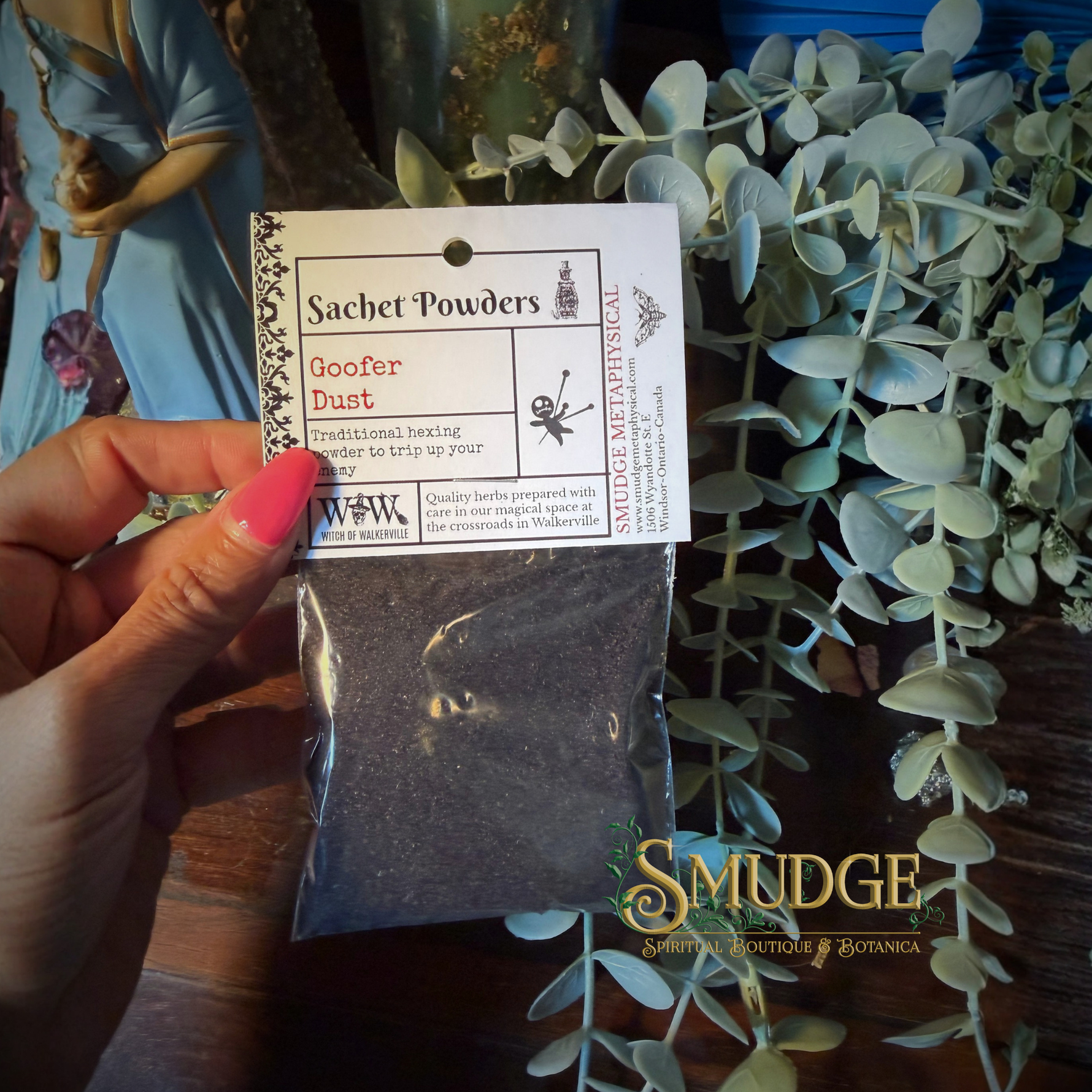 Hand holding a package of 'Goofer Dust' with a label in front of greenery