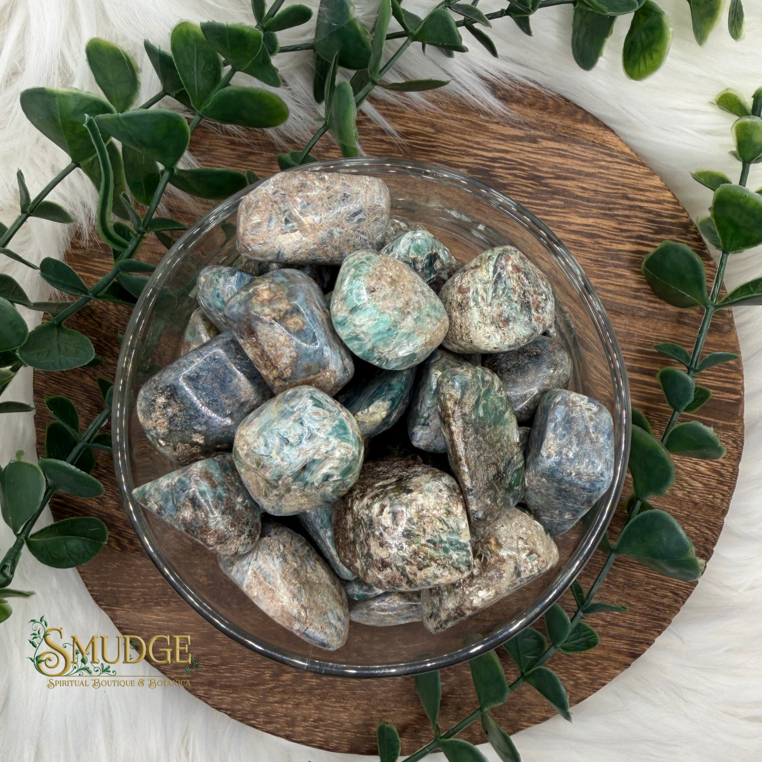 Glass bowl filled with tumbled stones on a wooden board with greenery