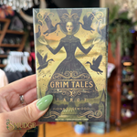 A hand with green nail polish holds a boxed tarot card deck titled "Grim Tales Tarot" by Fiona Edgewood. The box features an illustrated dark figure in a black dress with birds and gold decorative details on a muted gold background.