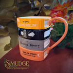 Haunted library mug on a table with a plant behind it.
