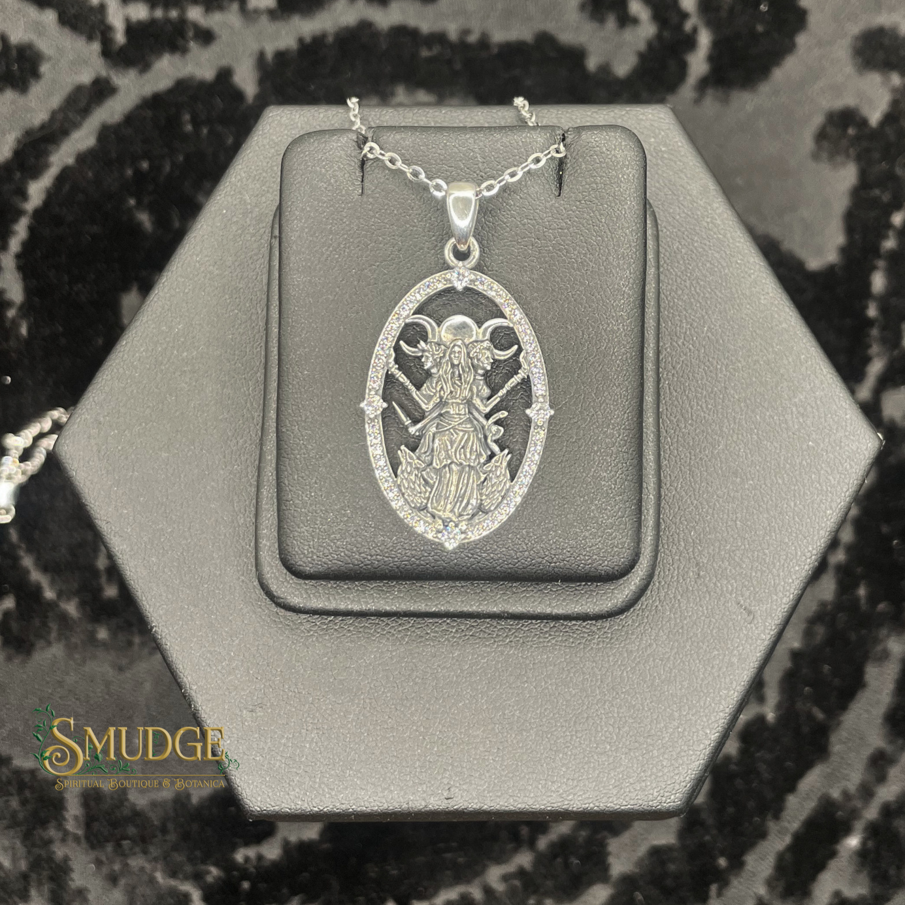 Silver pendant on a hexagonal gray stand with 'Smudge' branding.