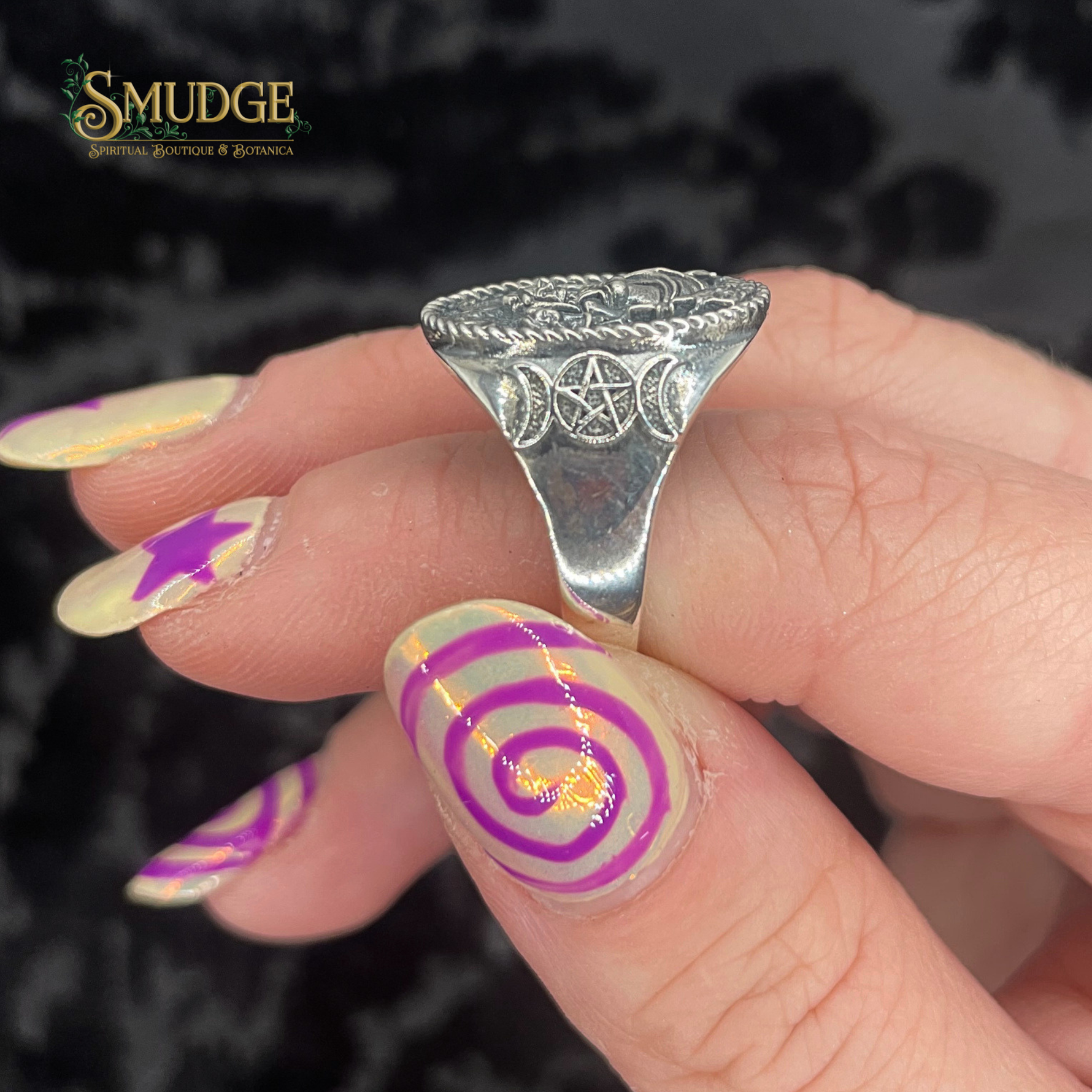 Silver ring with intricate design worn on a finger with colorful nail polish, against a dark background.