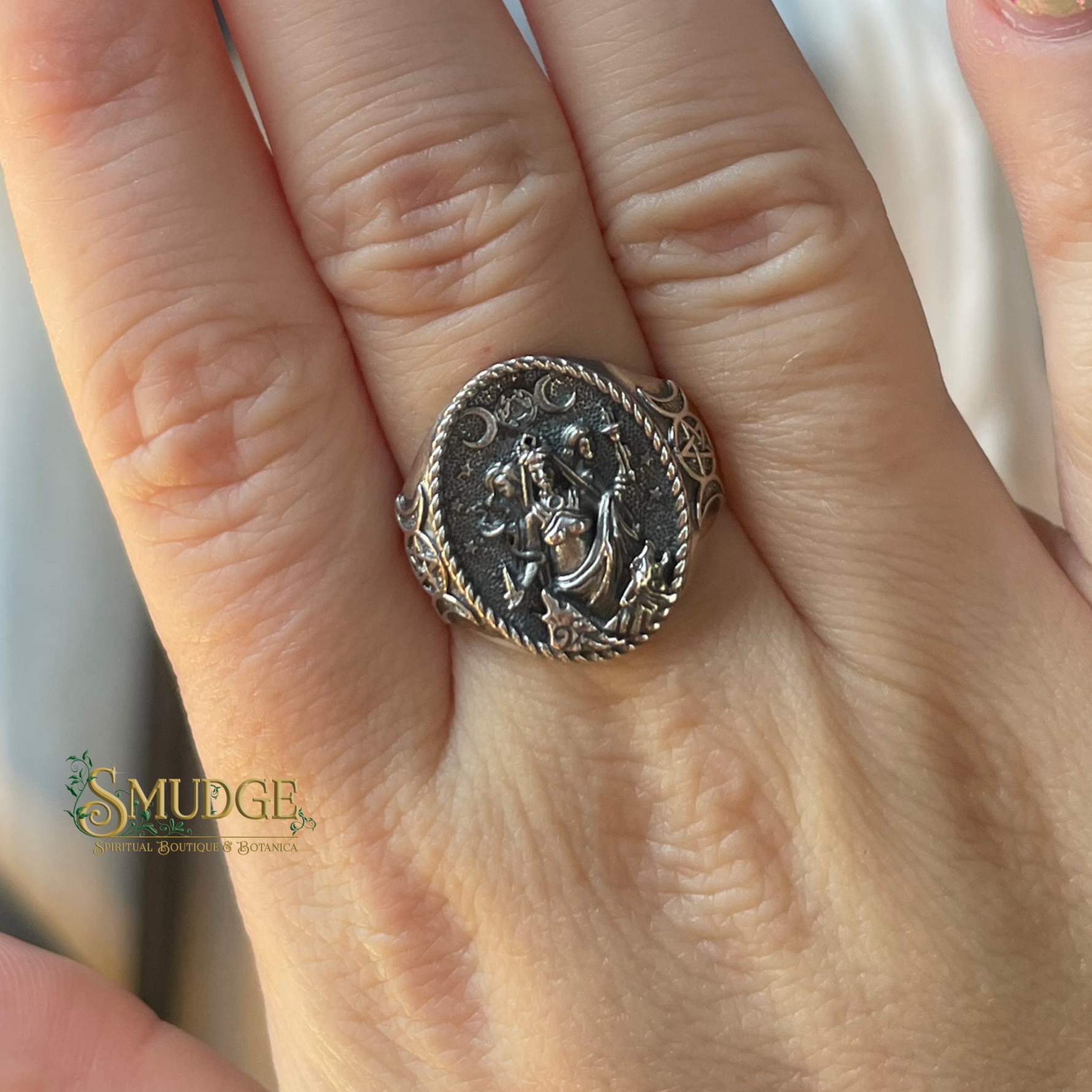 Silver ring with intricate design worn on a finger, branded 'Smudge'.