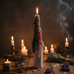 A tall, cylindrical white candle with a lit flame at the top and colorful dripping wax in red, blue, orange, yellow, and green around the sides, set against a plain light gray background.