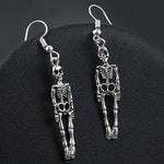 A pair of dangling skeleton earrings in silver-tone metal, displayed on a black textured surface.