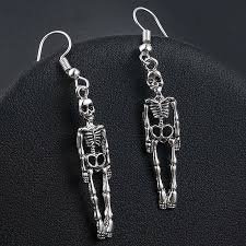 A pair of dangling skeleton earrings in silver-tone metal, displayed on a black textured surface.