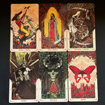 Six illustrated tarot-style cards arranged in two rows on a patterned fabric background. The cards feature Day of the Dead-inspired artwork with a rider on a horse, a robed figure in red and blue, a grim reaper with a scythe, skeletal figures, a skull in foliage, and a large red butterfly over a castle.