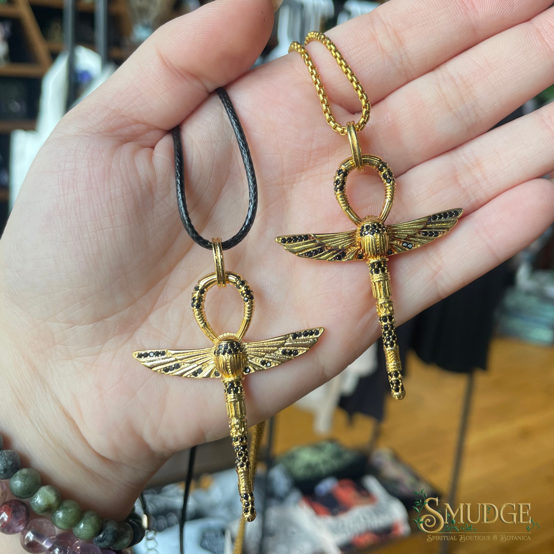 Two gold ankh pendants held in a hand with a blurred background