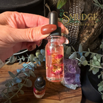 a hand holding a bottle of jezebel oil pink oil with roses in it.